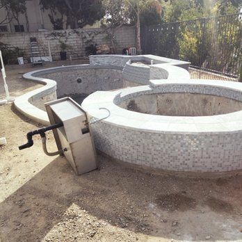 Pool under construction with tiled edges, a spa, and equipment, outdoors in a yard.