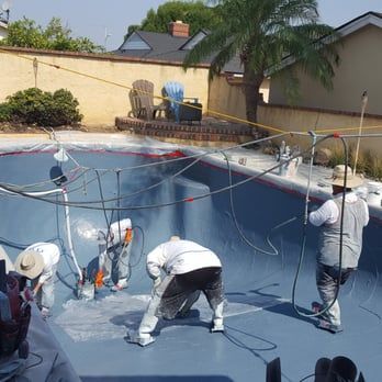Workers spray painting a blue interior of an empty swimming pool.