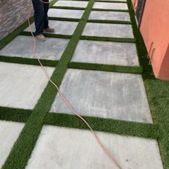 Concrete pavers with artificial turf in between. Person holding a wire in the background.