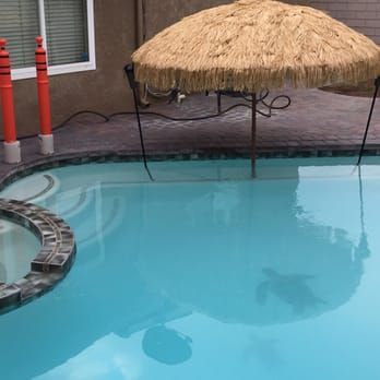 A pool with bright blue water, a tiki umbrella, and a shadow of a person swimming.