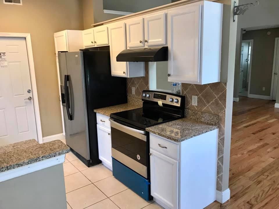 Kitchen with white cabinets, black appliances, granite countertops, tile backsplash, and wooden floors.