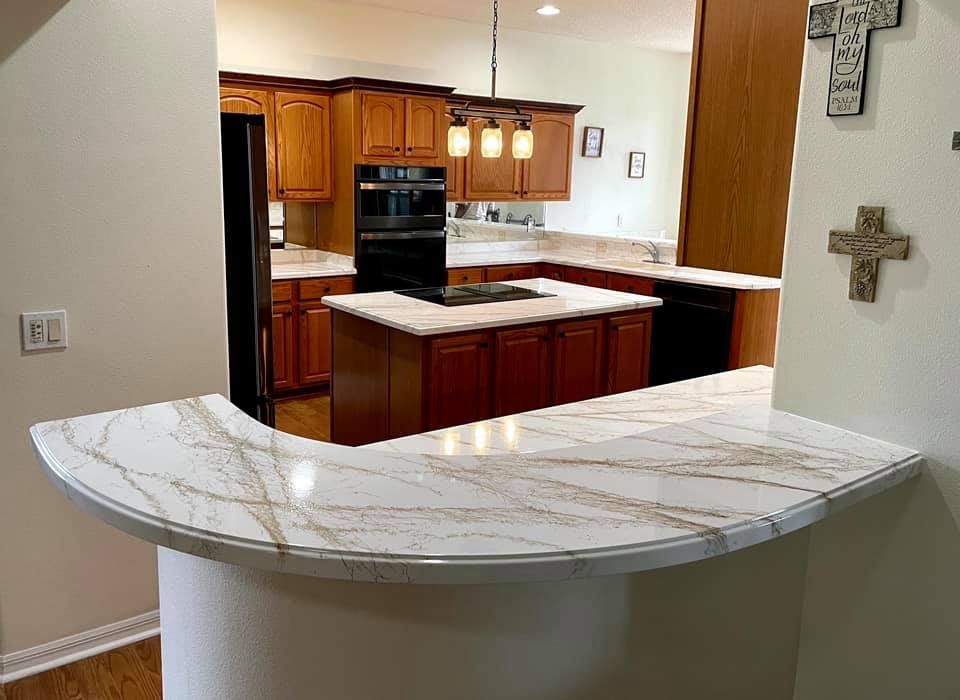 Kitchen with a white and gold countertop, dark cabinets, and an island.