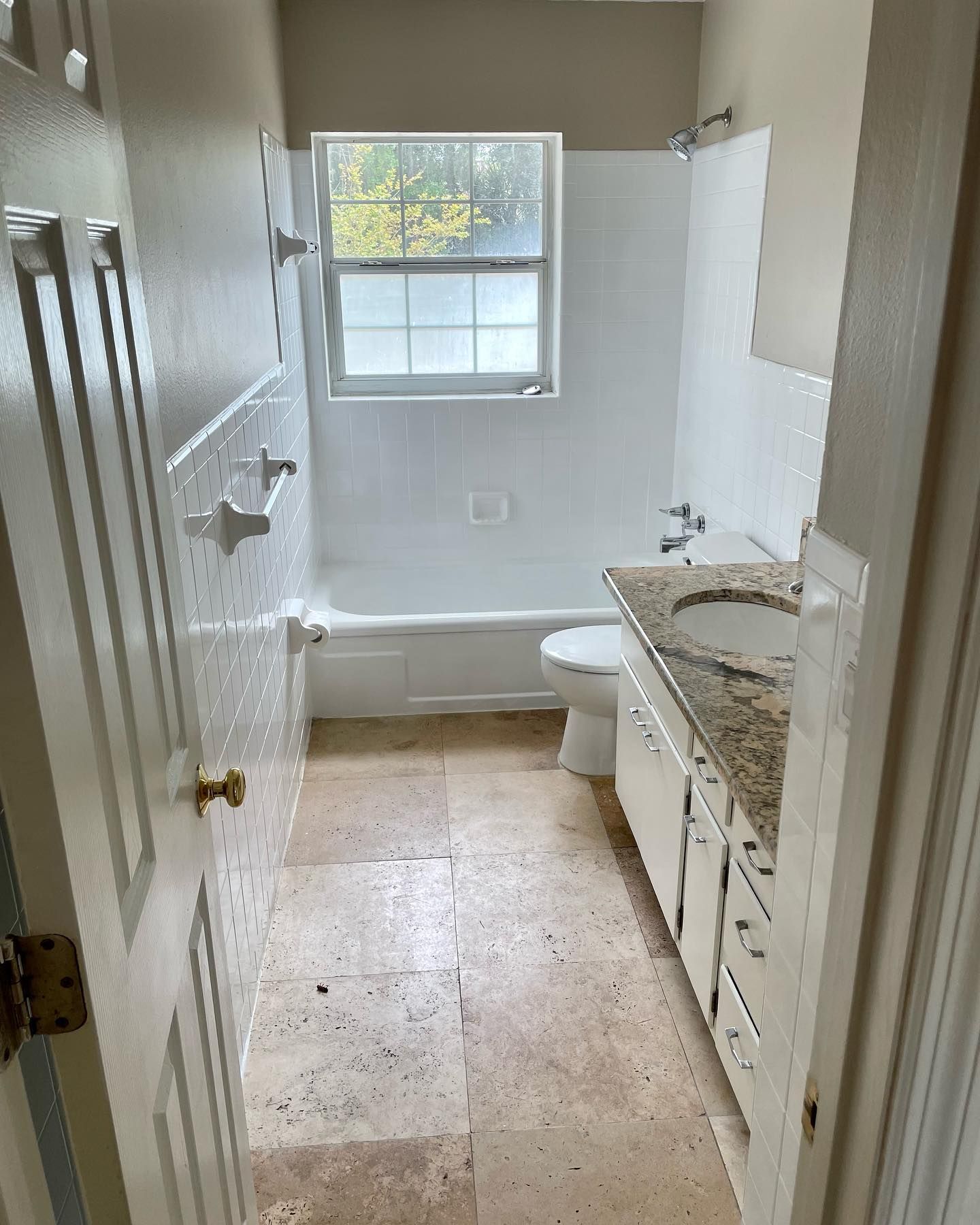 Bathroom with white tile, vanity, and tan floor. Window above the tub.