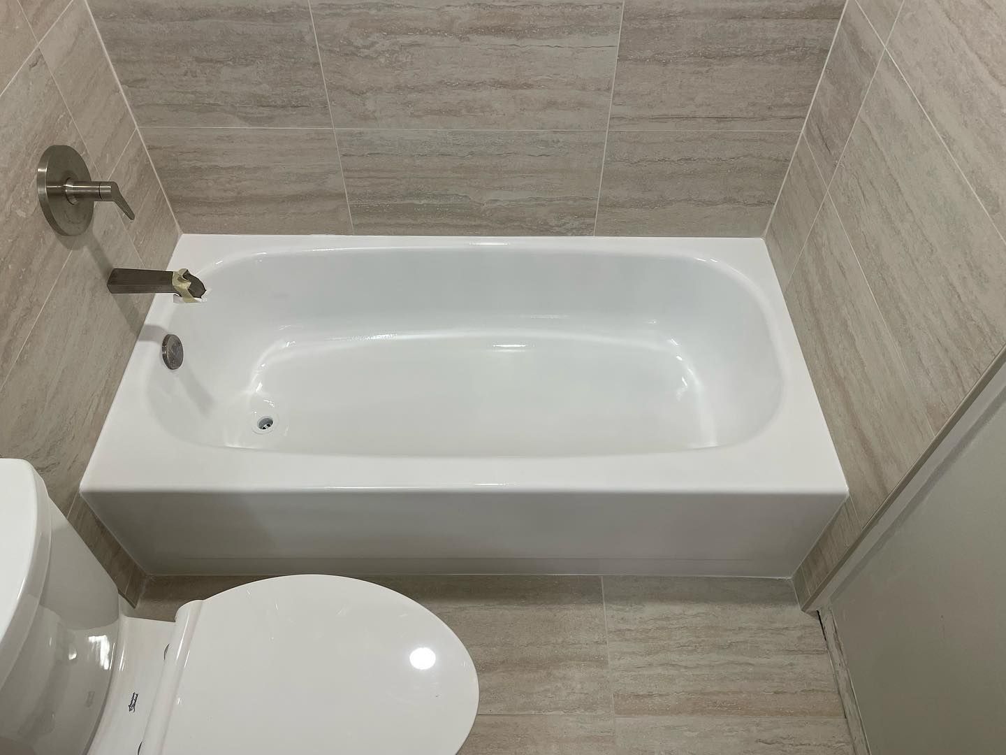Bathtub and toilet in bathroom with beige tile walls and flooring.