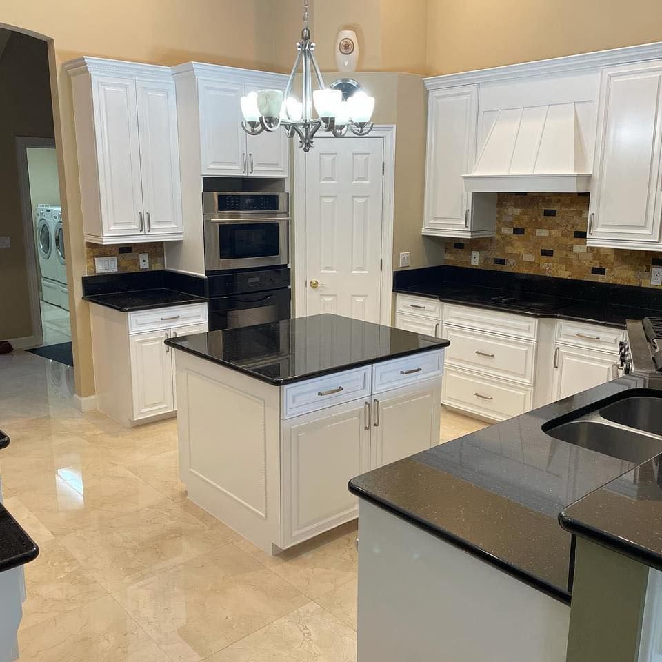 White kitchen with black countertops and island, stainless steel appliances, and a hanging chandelier.