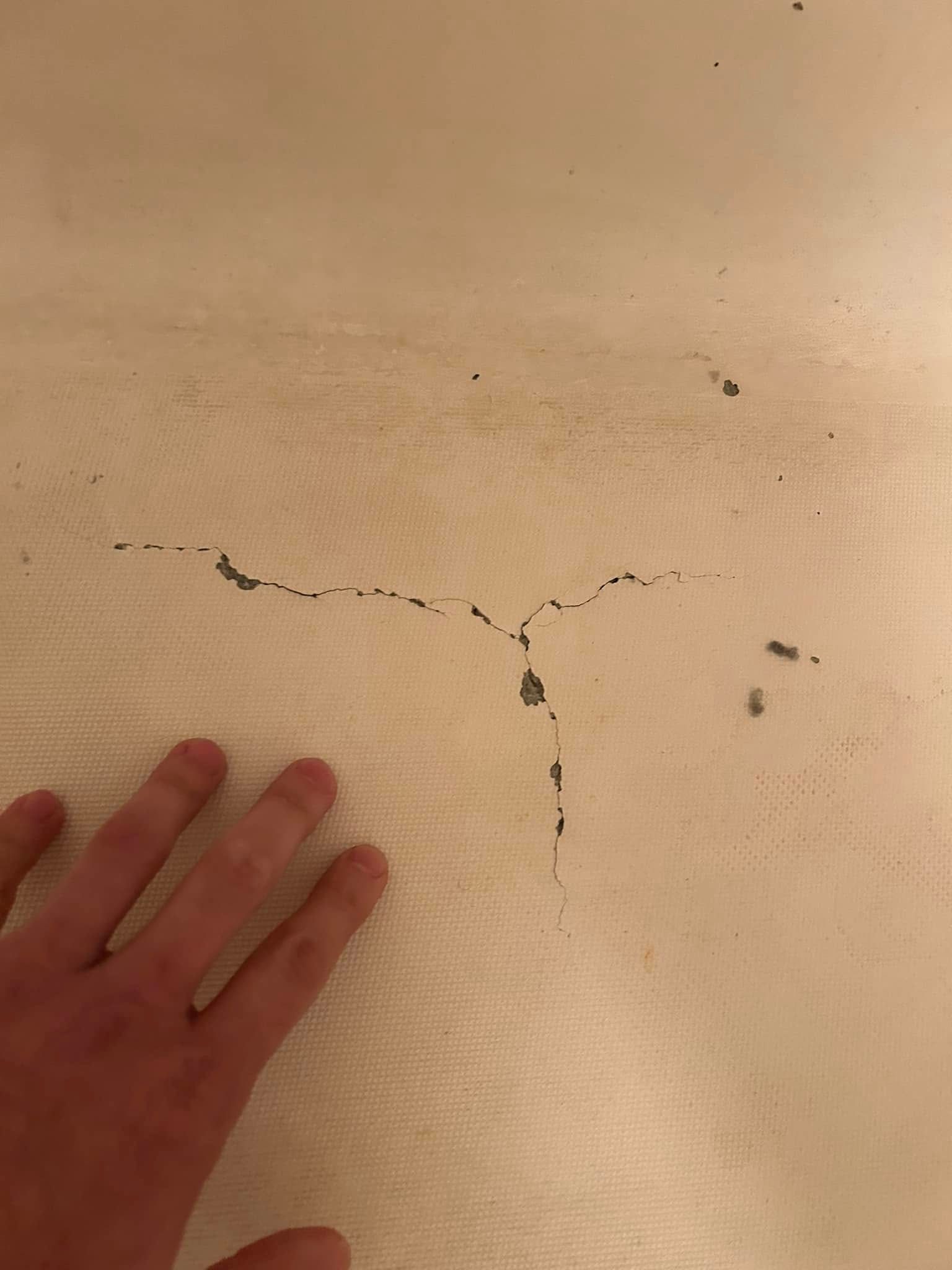 Hand next to a cracked surface, possibly a bathtub, with dark discoloration in the cracks.