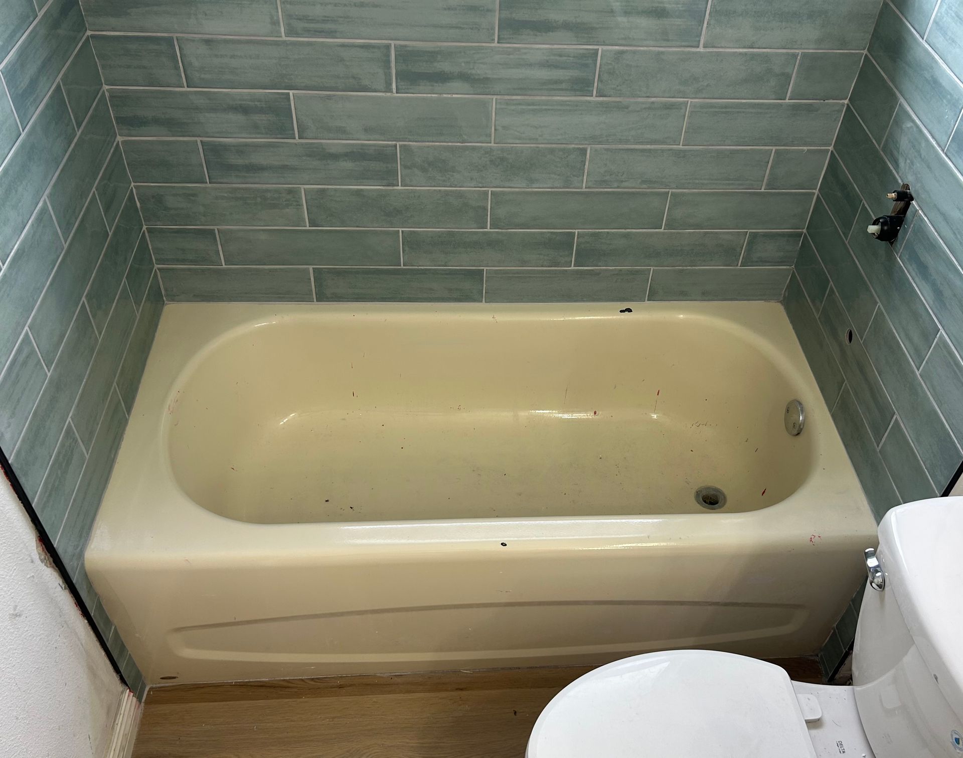 Bathtub with light-colored walls, surrounded by blue-green tiled wall. A toilet is positioned to the side.