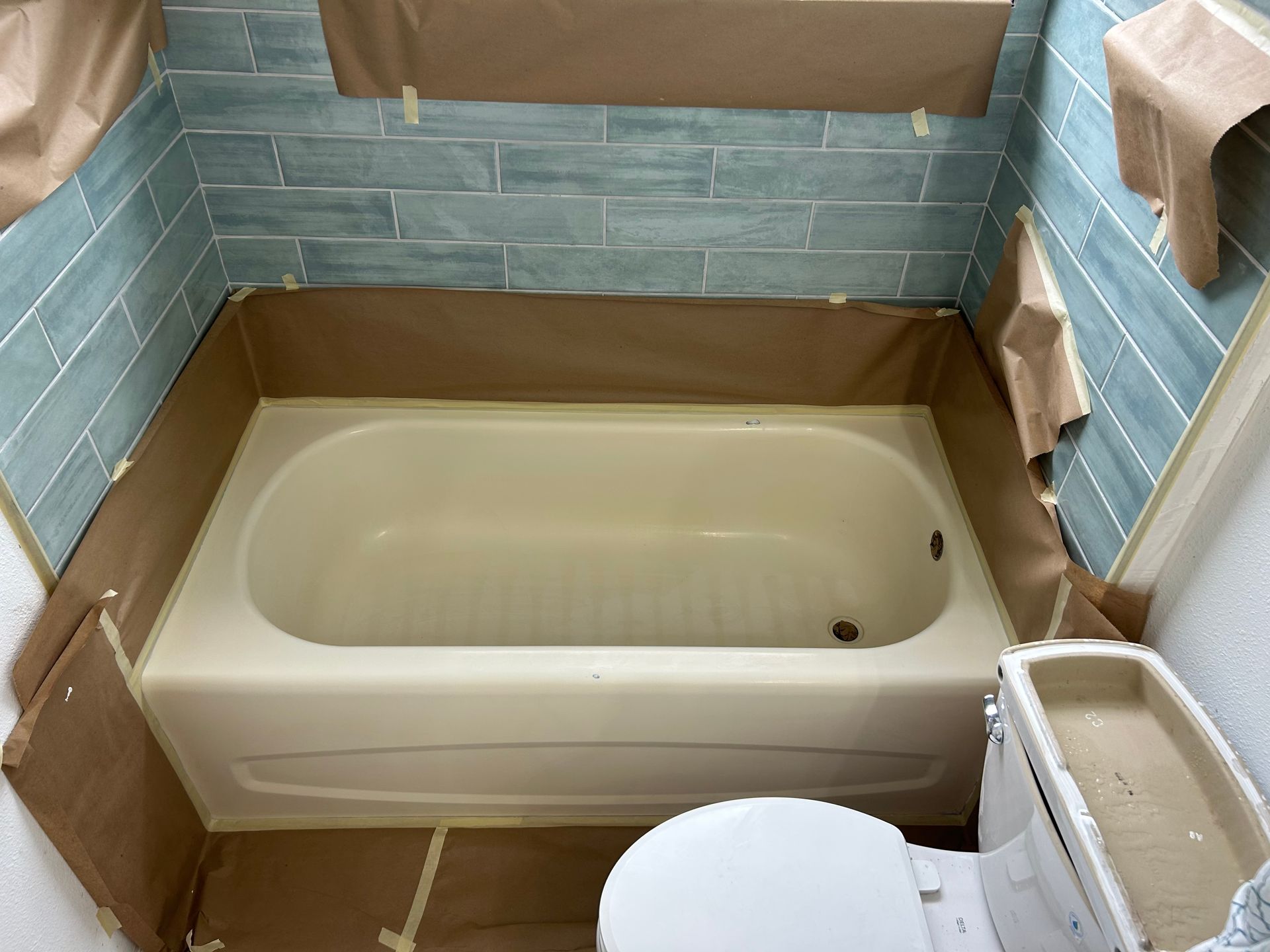 Bathroom with tub and blue tile, masked for painting, tan paper covering tub and walls.