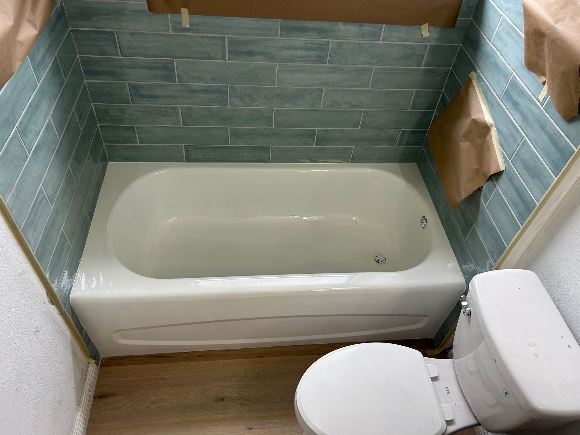 Bathroom with teal tiled walls, white bathtub, and toilet.