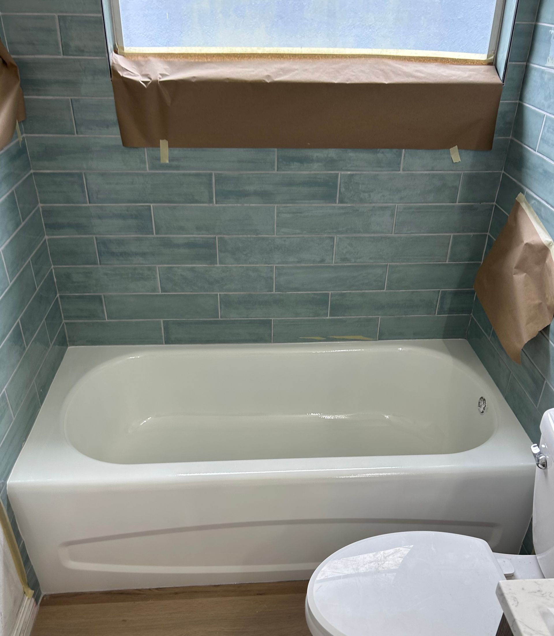Bathroom with white bathtub, blue tile, and toilet, seen from the front.