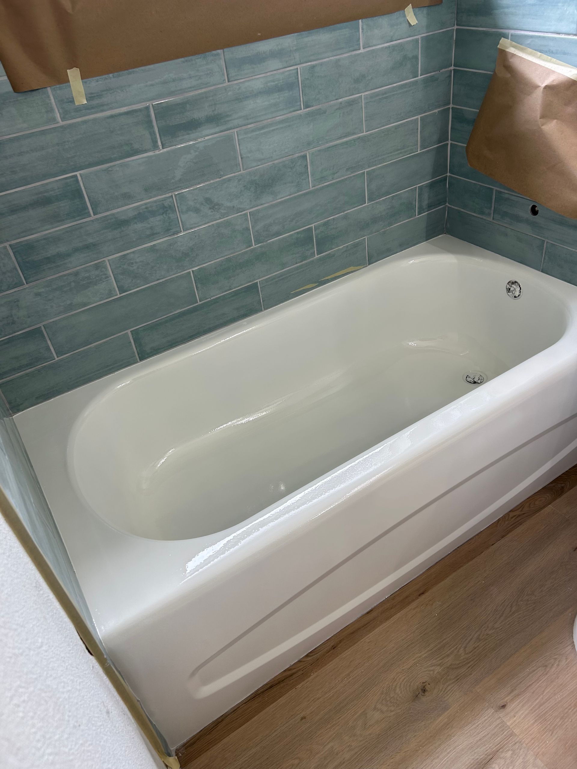White bathtub with blue tile surround, in a bathroom.