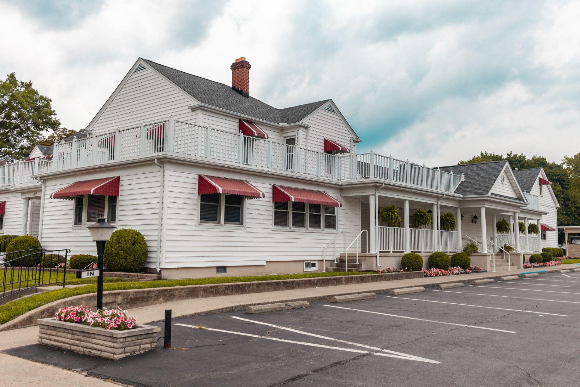 A large white house with red awnings and a parking lot in front of it.