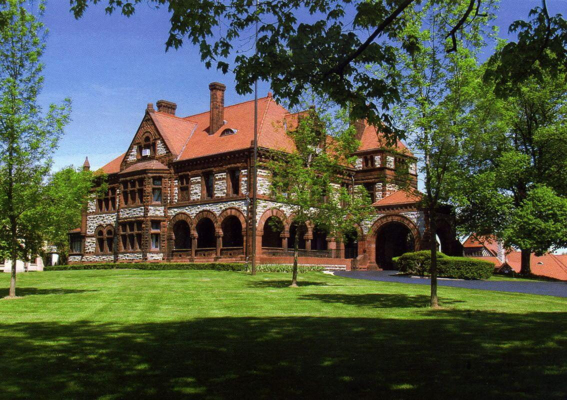 A large brick building with a red roof is surrounded by trees