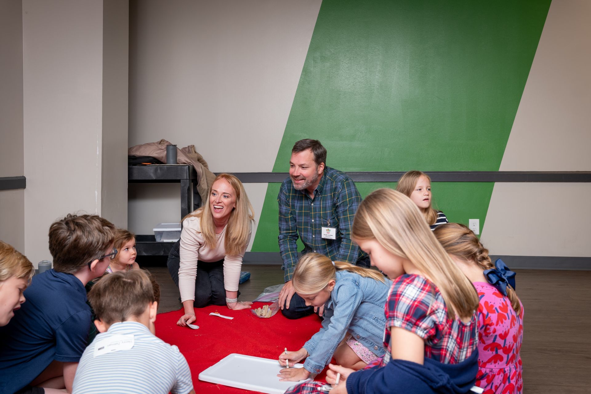 People gathered around a red tablecloth, writing and talking in a classroom or workshop setting