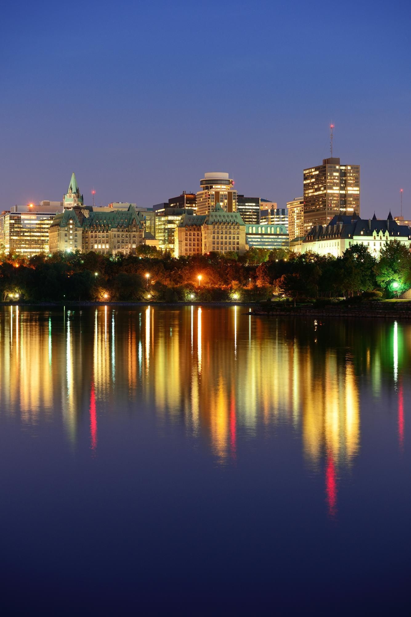 City skyline at dusk with lights reflecting on water.