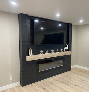 Black shiplap accent wall with TV, fireplace, and decorative shelf. Beige walls, light wood floor.