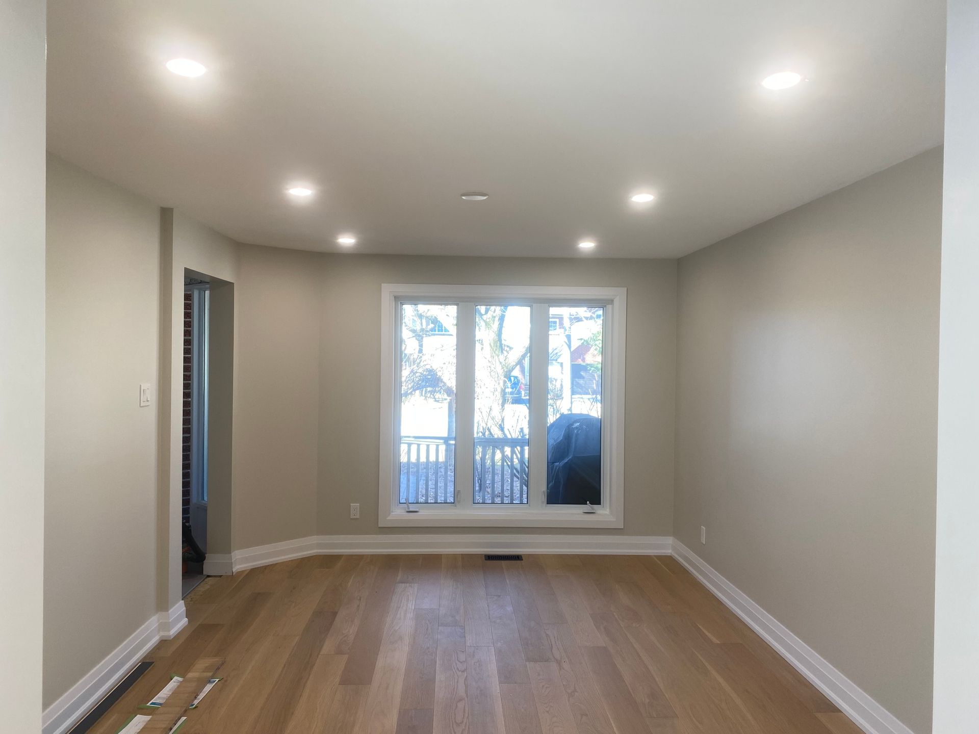 Empty room with light wood floors, recessed lighting, and a large window.