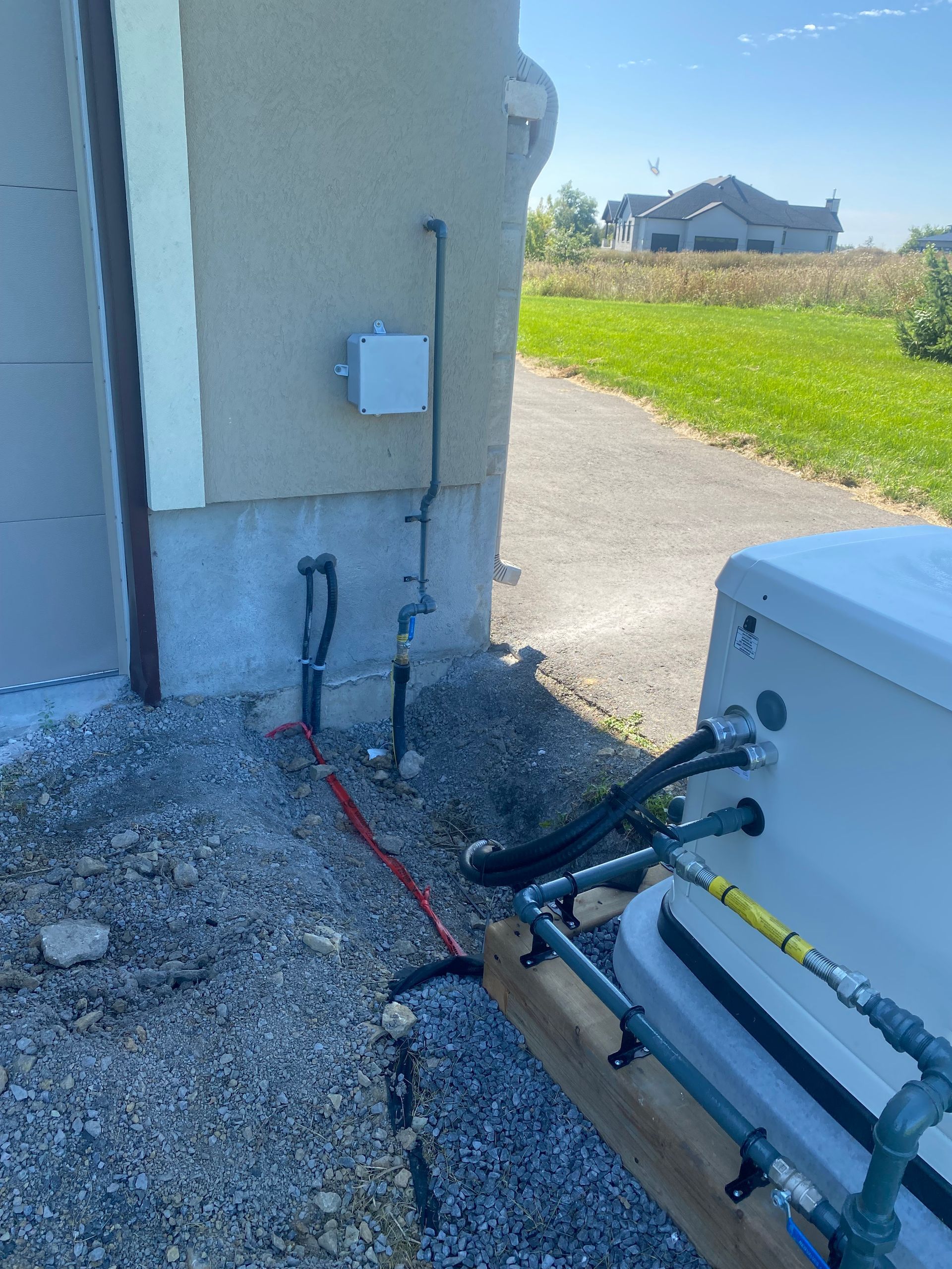 Exterior view of building with equipment, grey pipes and wires near a gravel area and driveway.