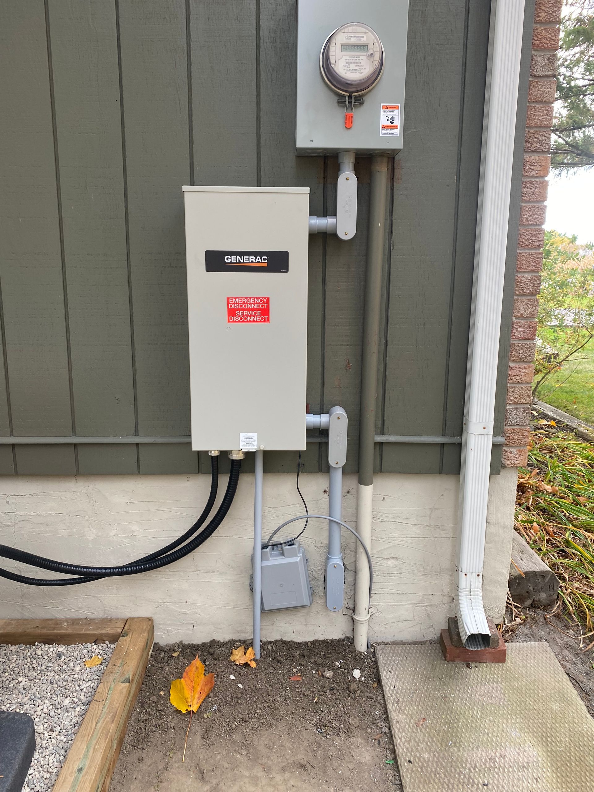 Electrical panel mounted on a green building wall with meter and conduit. Concrete pad, and gutter present.