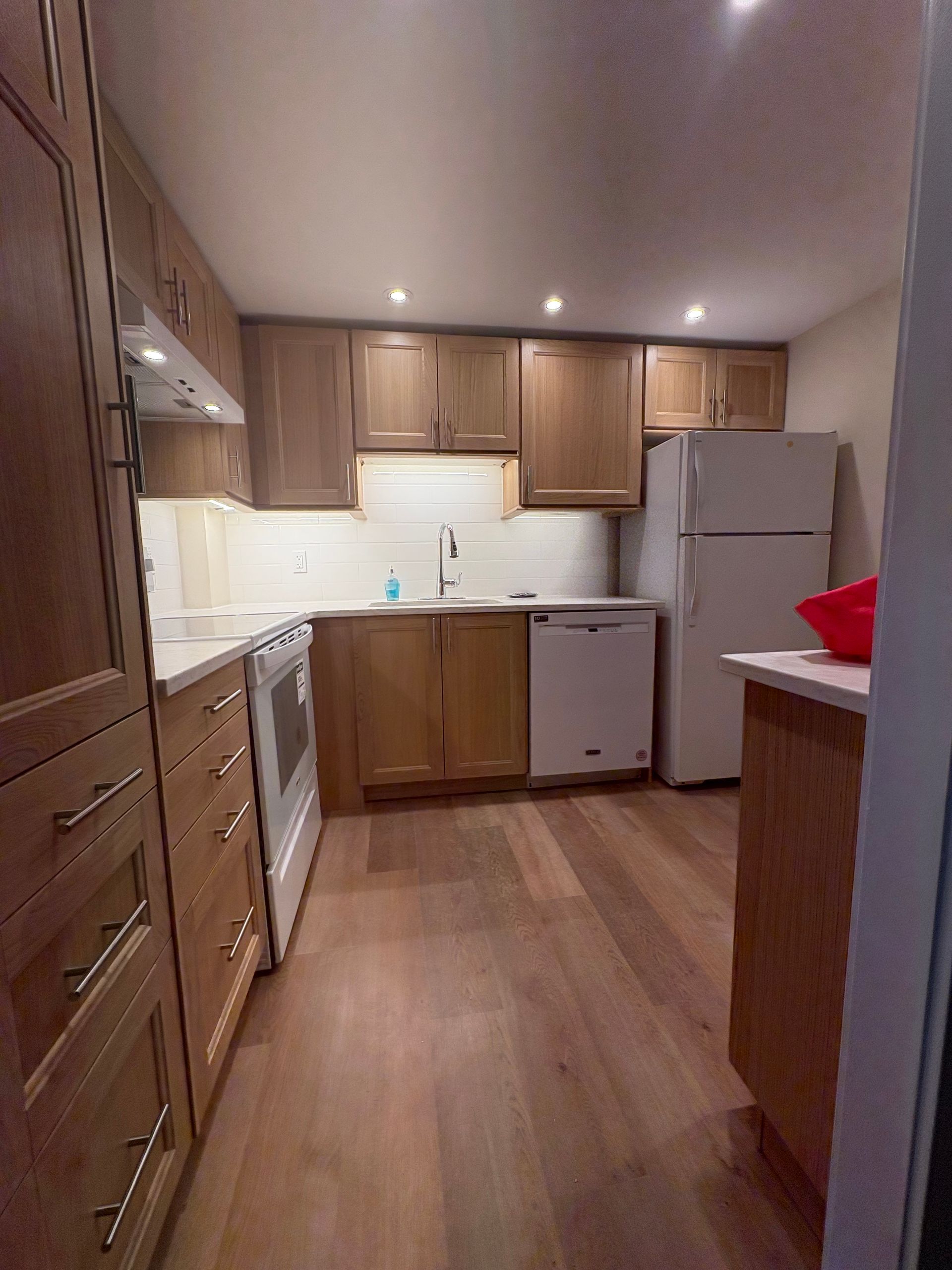 Wooden kitchen with light-colored cabinets, white appliances, and hardwood floors.