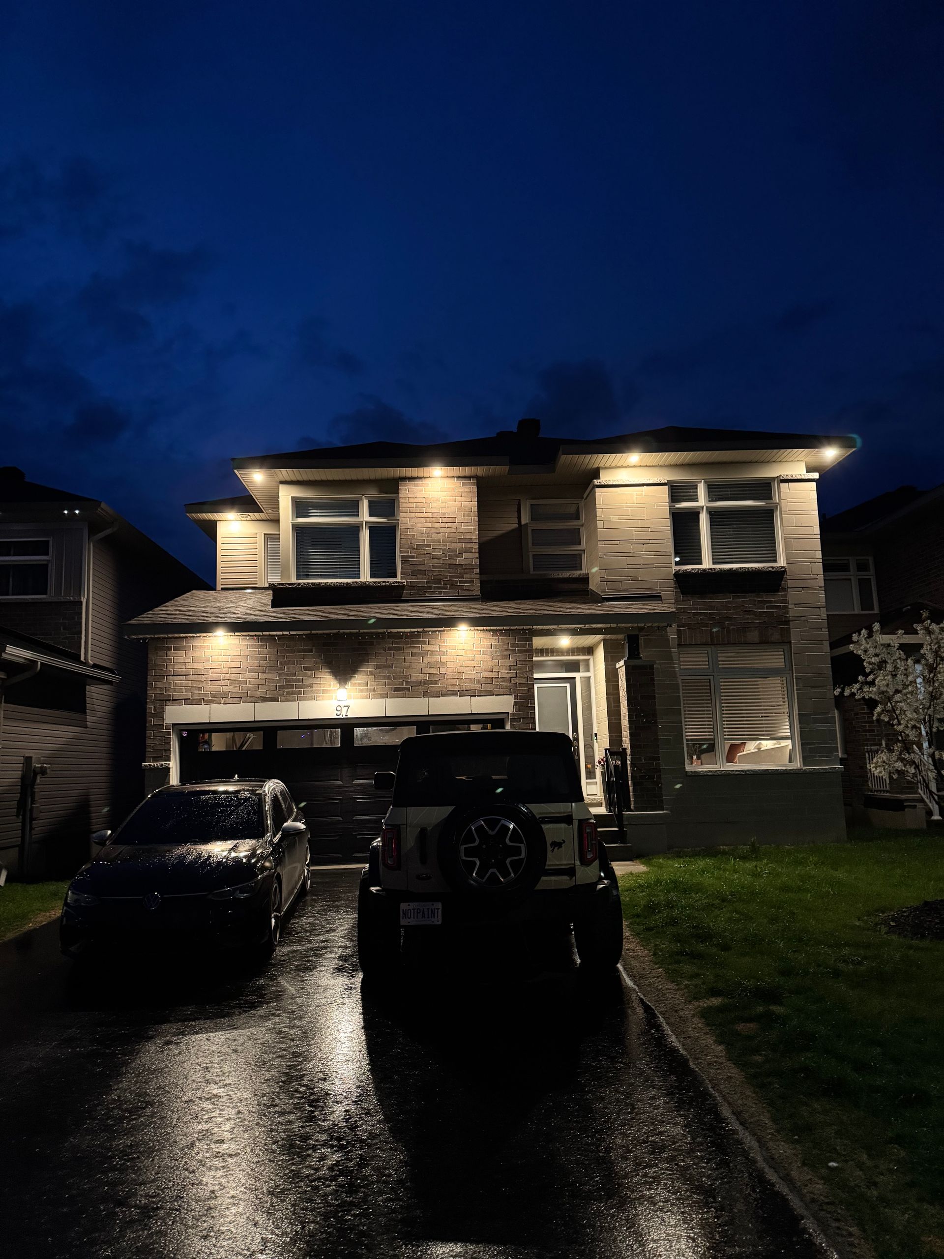 Two-story house at night with illuminated facade, cars parked on driveway.