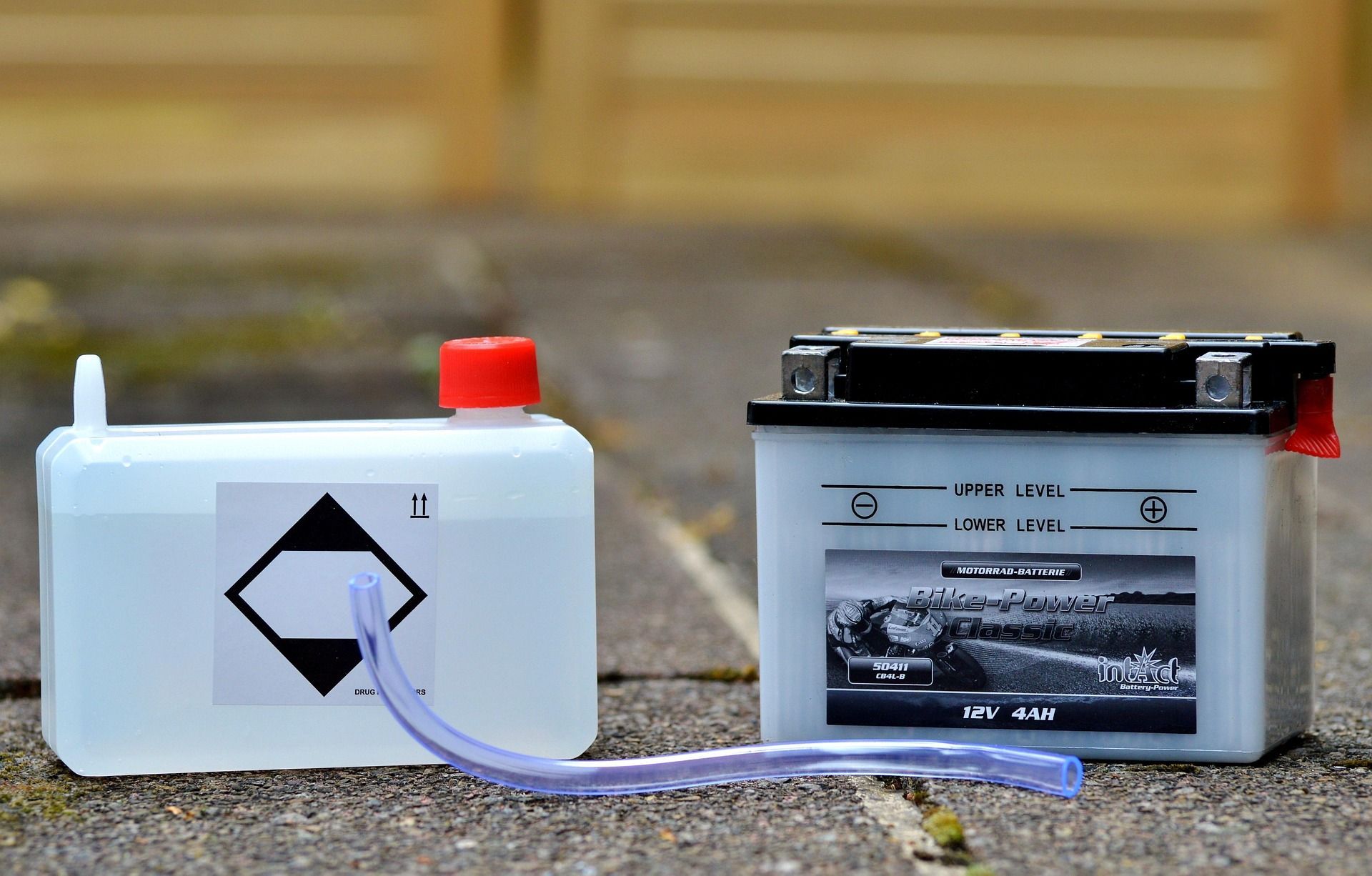 Battery and fluid container on a stone surface; container has hazard symbol and tubing.