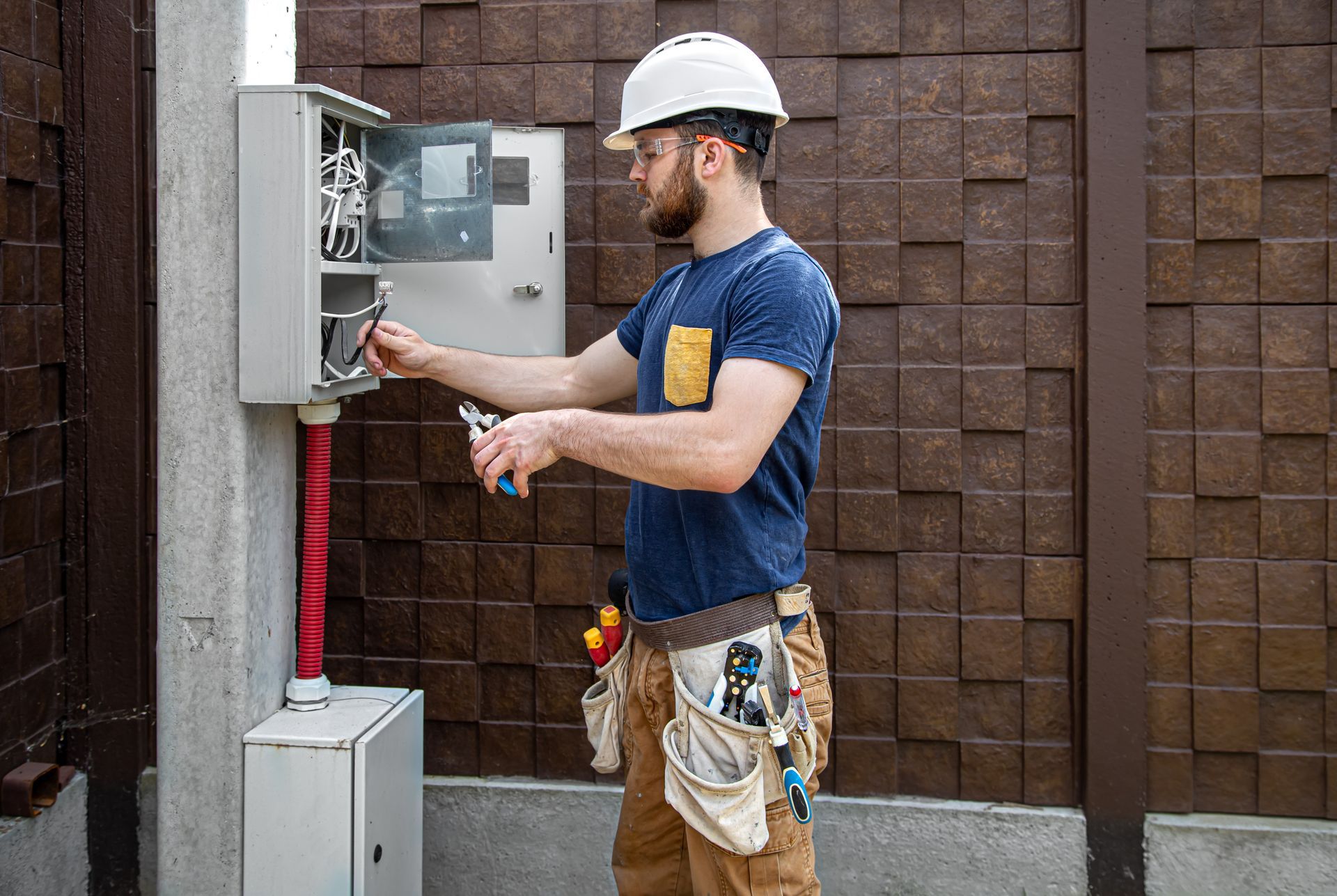 Electrician in a hard hat working on an electrical panel outside.
