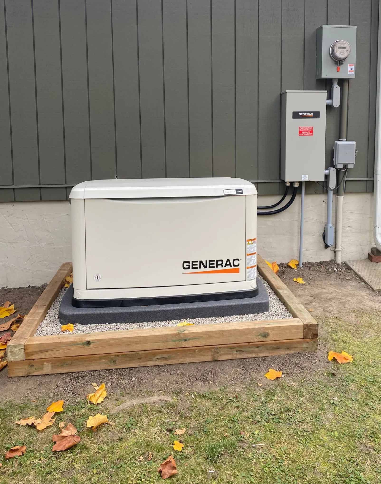 Generac generator on a gravel base next to a house with electrical components. Fall leaves are scattered nearby.