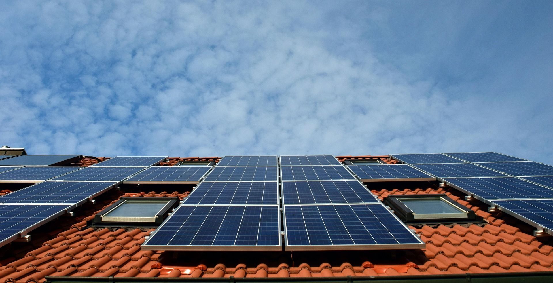 Solar panels on a red tile roof with a blue sky and scattered clouds.