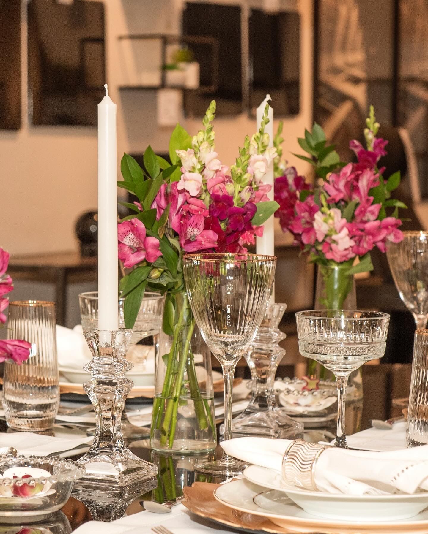 Uma mesa posta com pratos, velas, taças de vinho e vasos de flores.