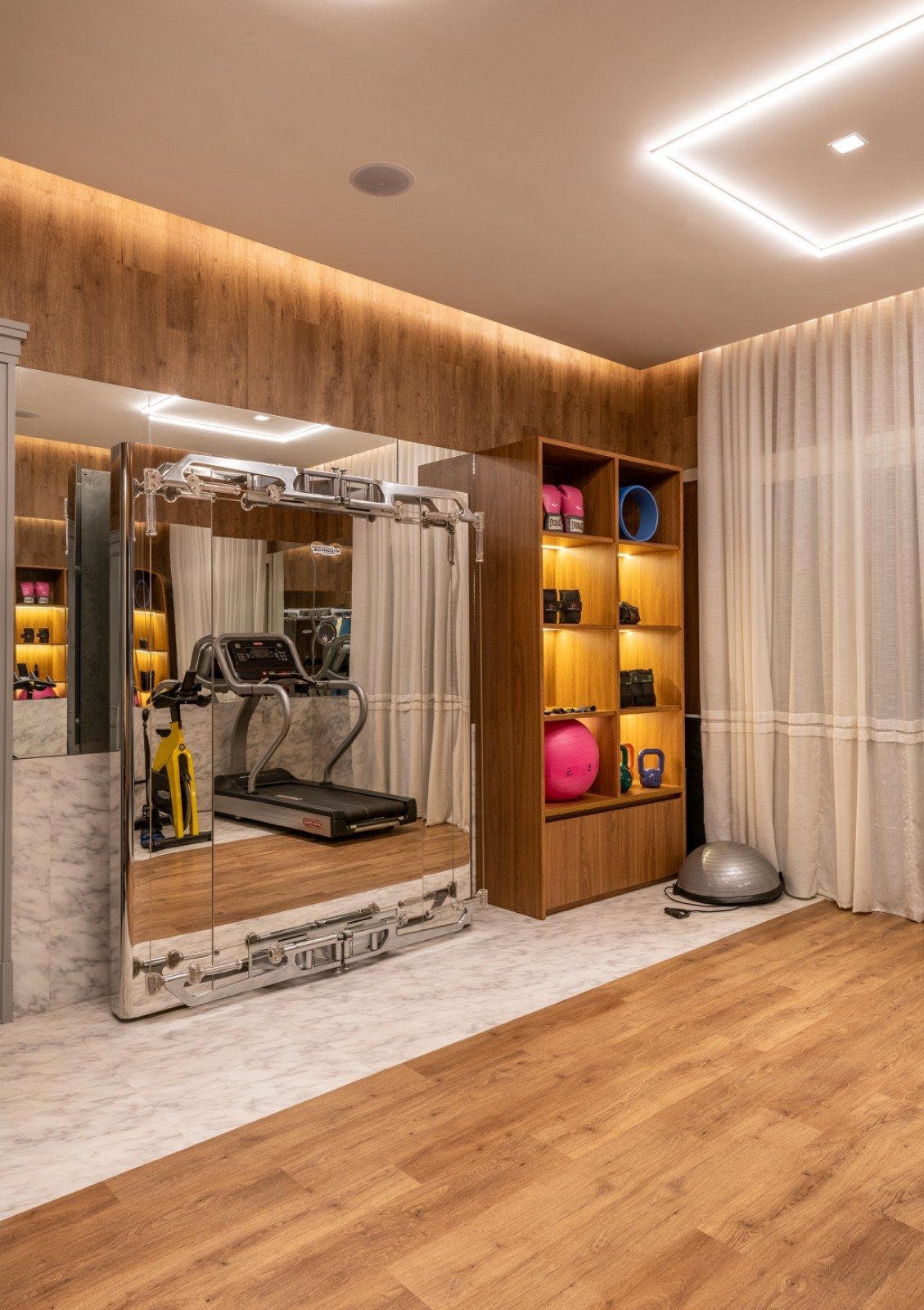 Uma academia em casa com uma esteira e um espelho grande.