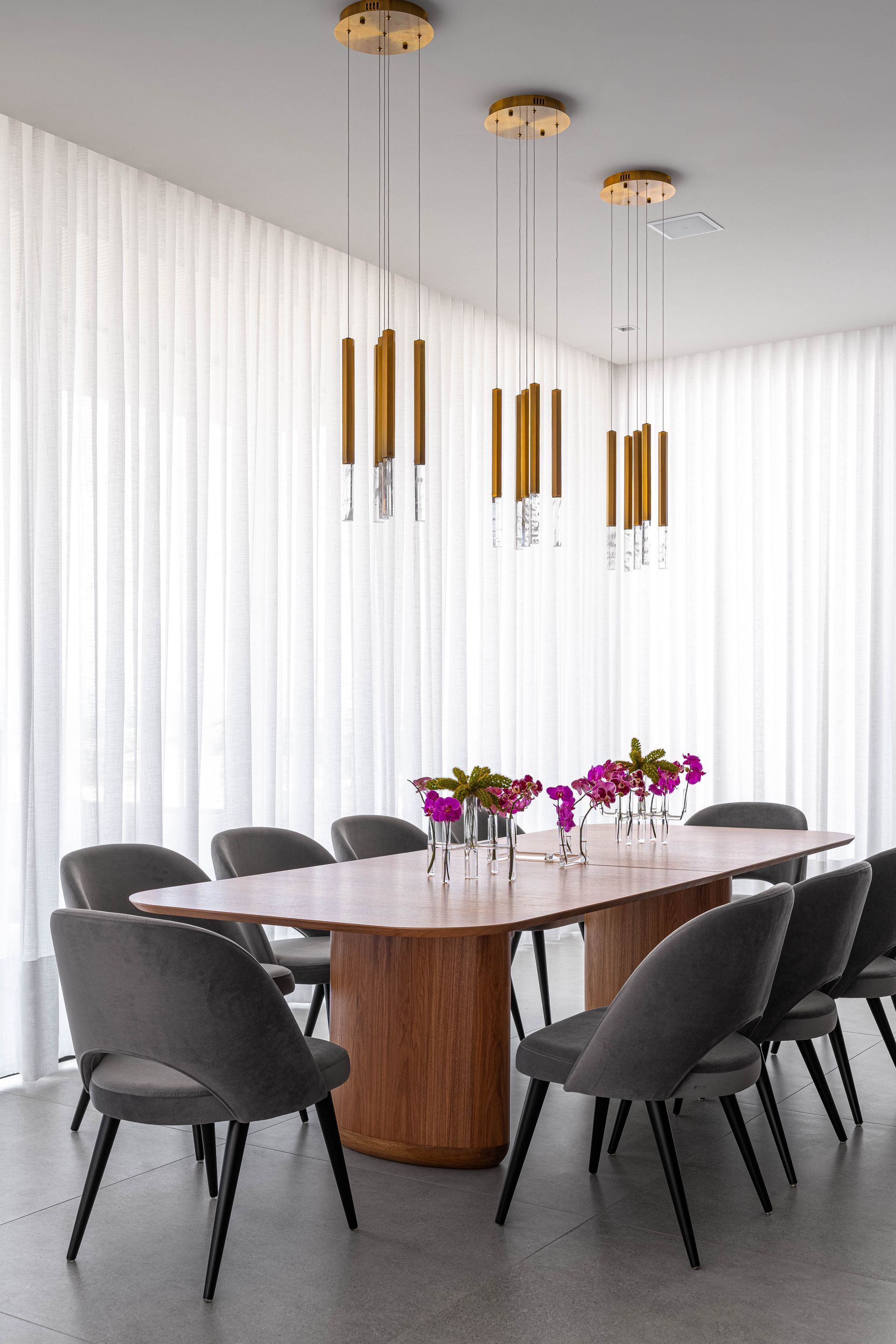 Uma sala de jantar com uma longa mesa de madeira e cadeiras cinzas.