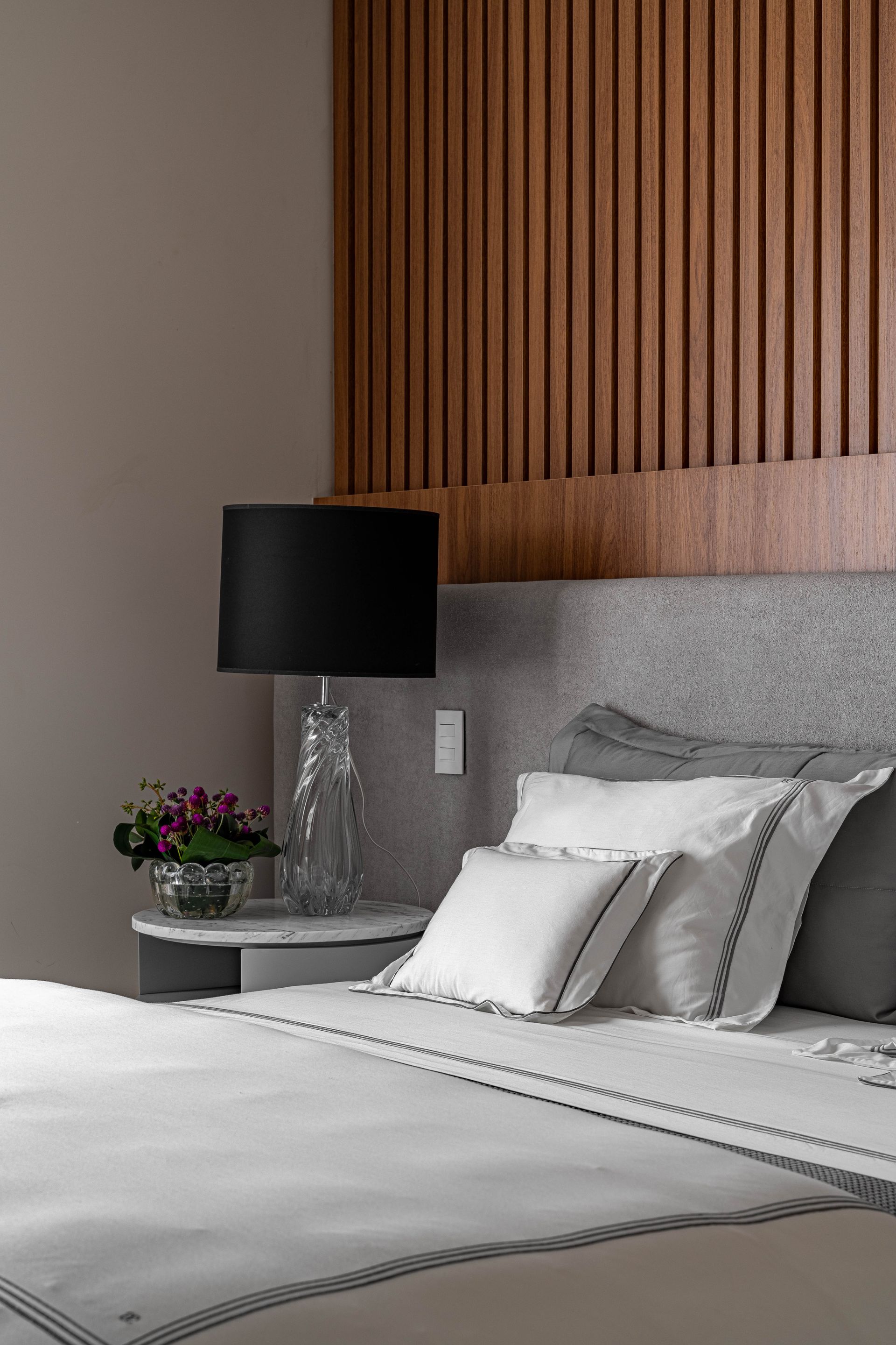 Um quarto com cama, mesa de cabeceira, abajur e cabeceira de madeira.