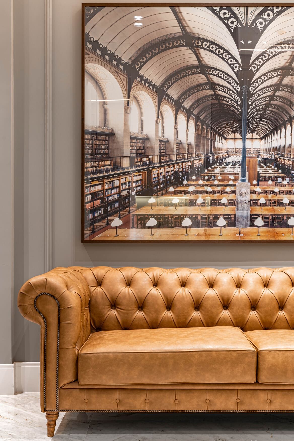 Um sofá de couro marrom está sentado em frente a uma grande pintura de uma biblioteca.