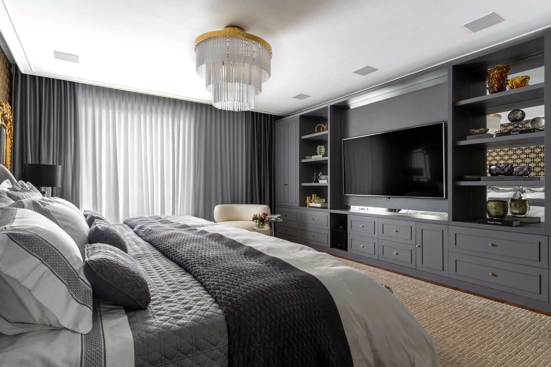 Um quarto com uma cama, televisão, prateleiras e um lustre.