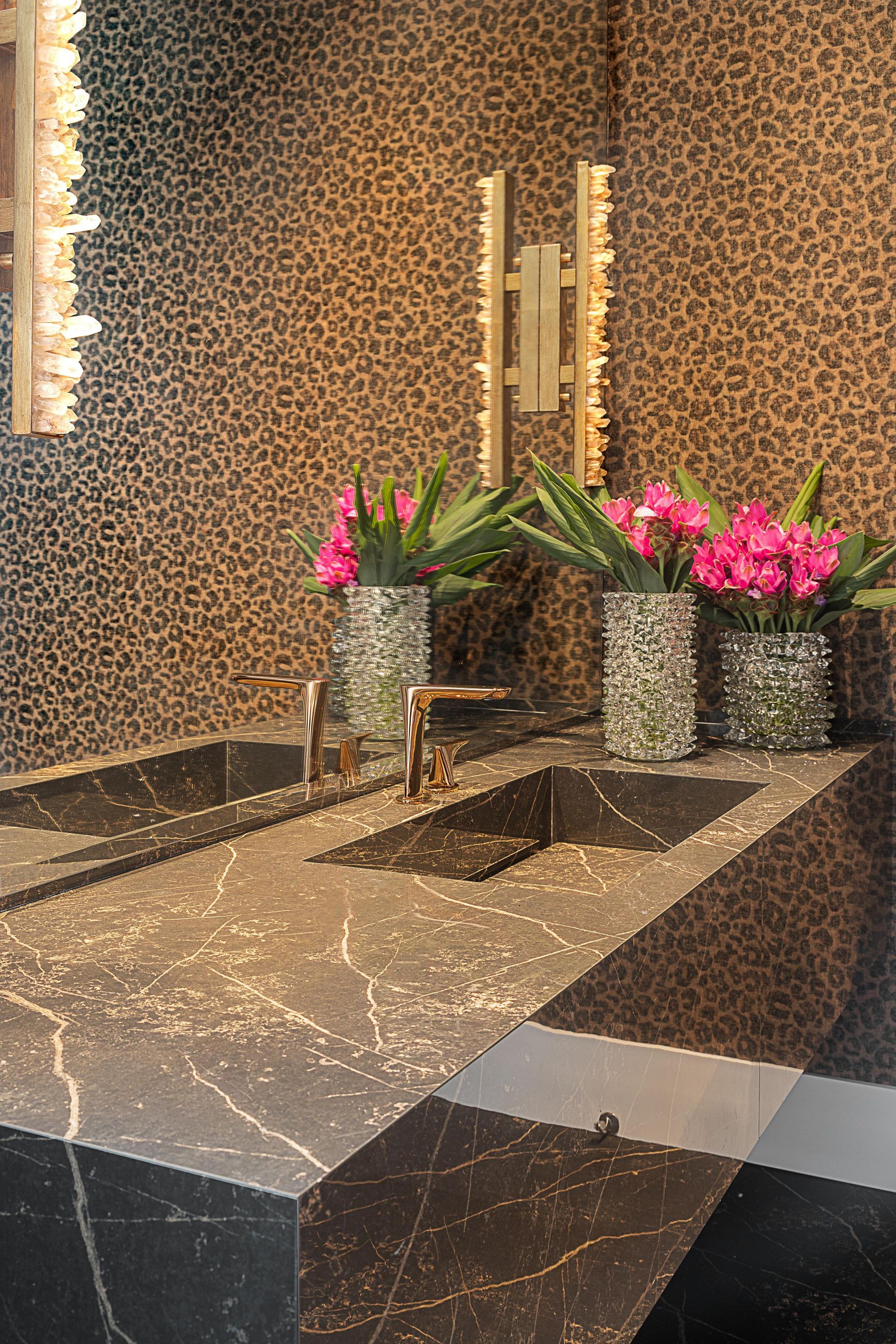 Um banheiro com duas pias, um espelho e flores em vasos.