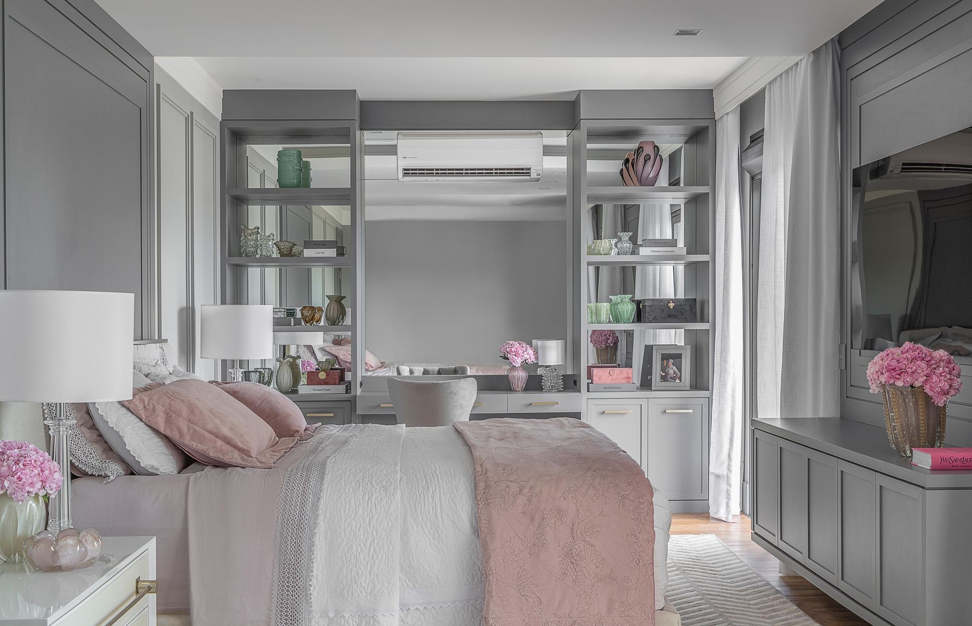 Um quarto com uma cama, mesa de cabeceira, abajures, prateleiras e uma televisão.