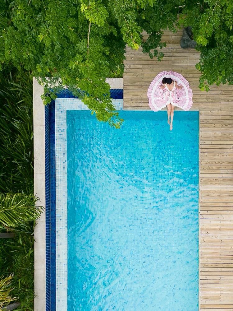 Uma vista aérea de uma mulher flutuando em uma jangada rosa em uma piscina.