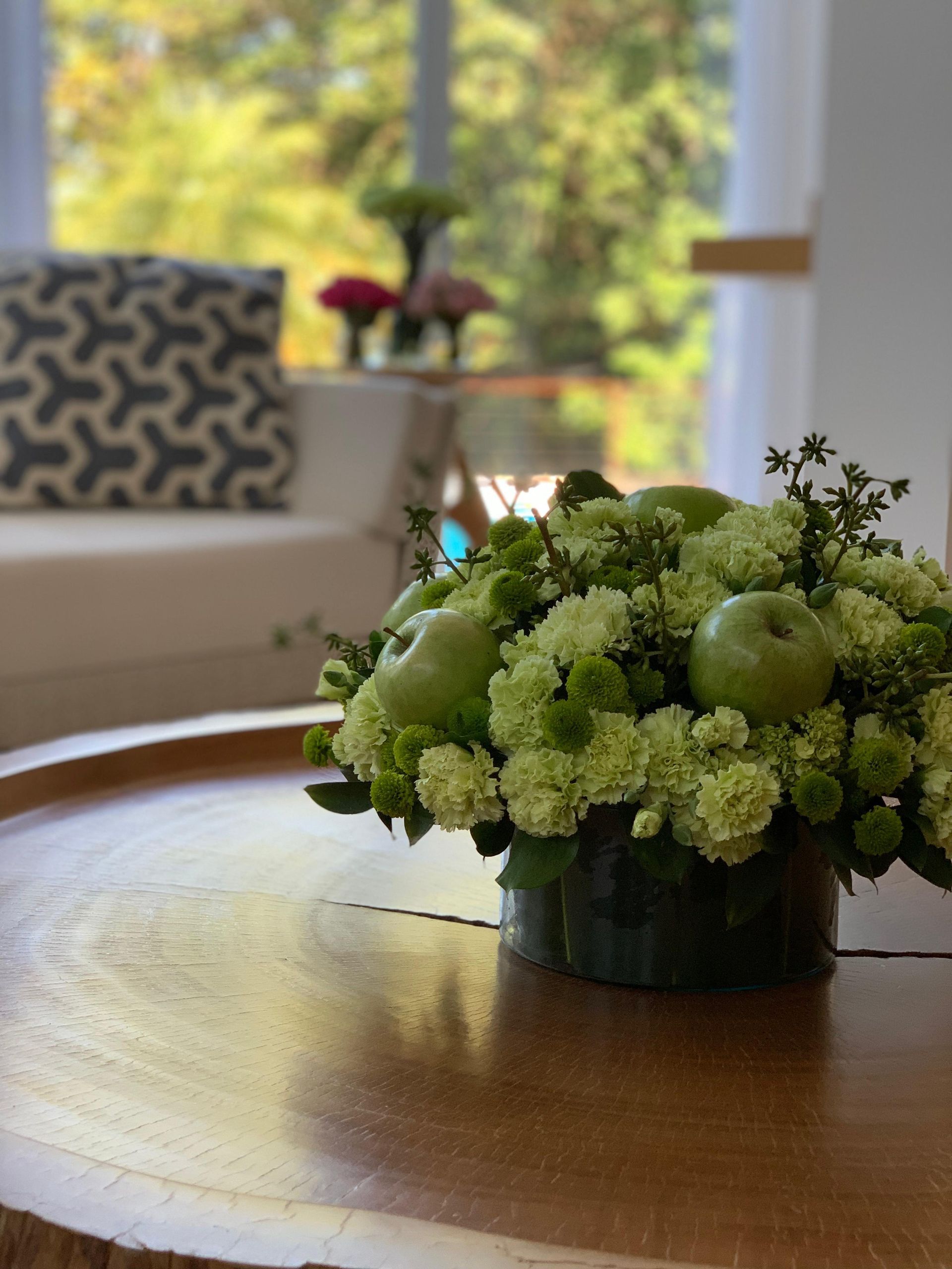 Um vaso de flores verdes e maçãs sobre uma mesa de madeira