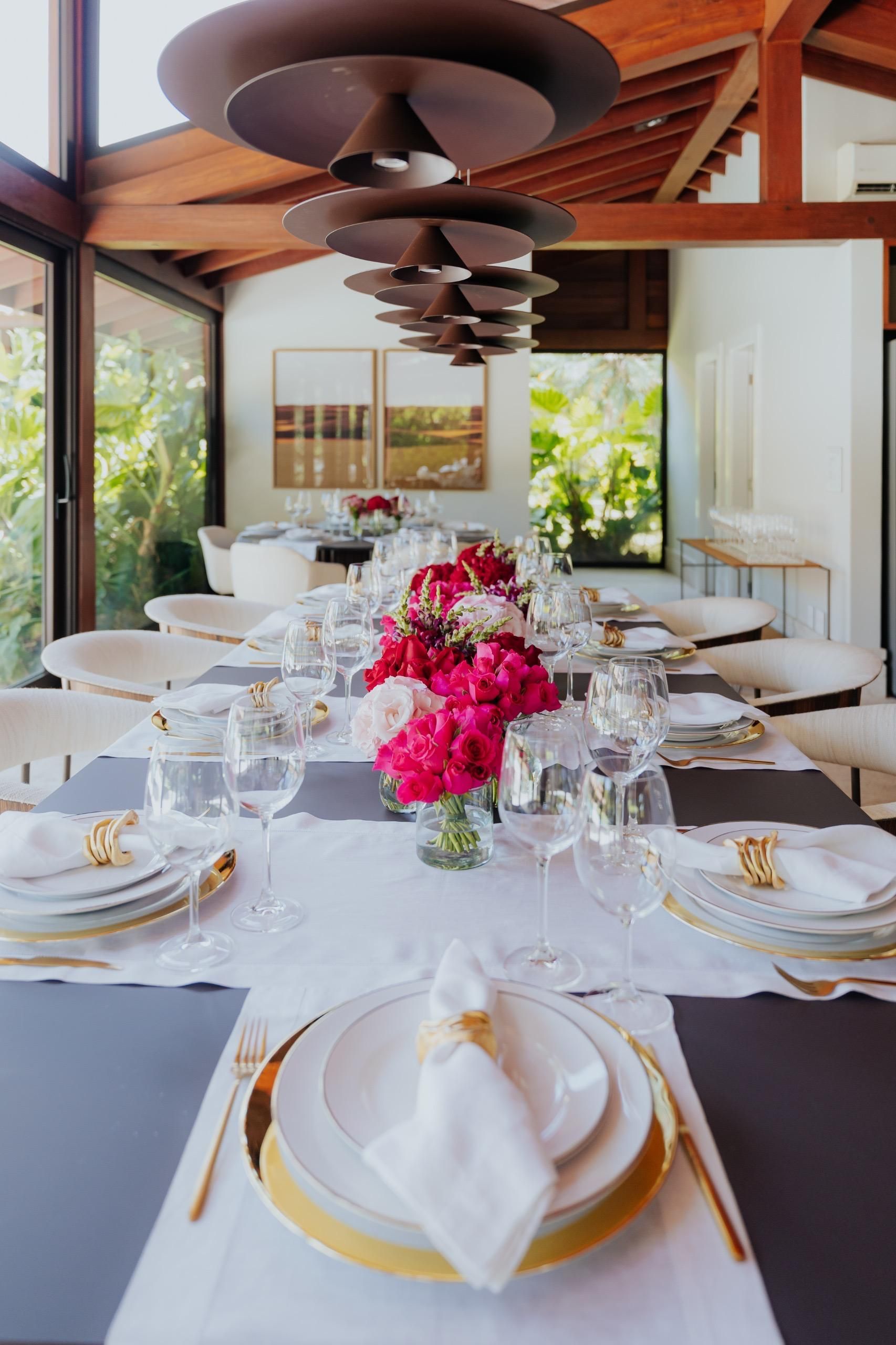 Uma longa mesa de jantar com pratos, utensílios e flores.