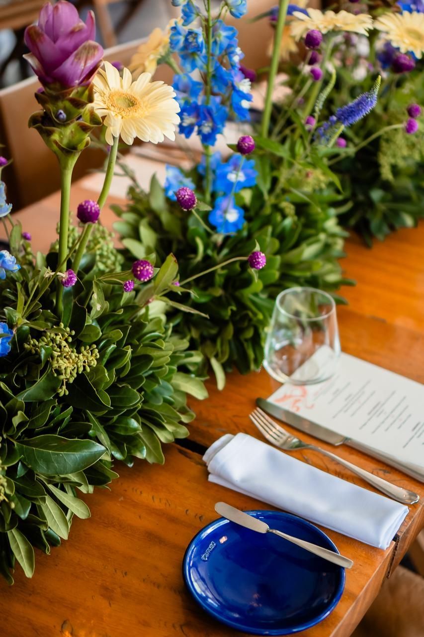 Uma mesa de madeira com um prato azul, talheres e flores sobre ela.