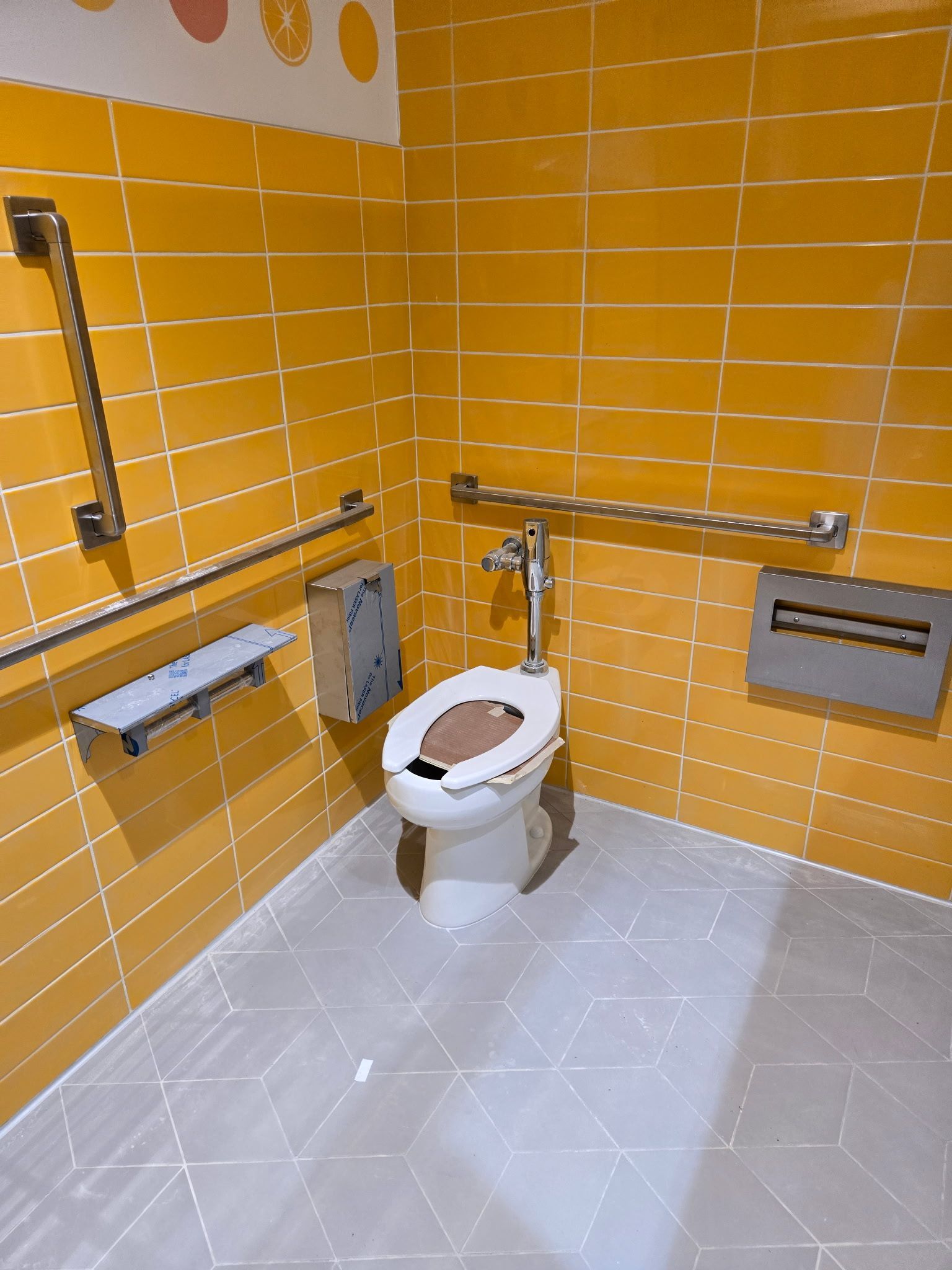 Group of people smiling at an outdoor bar, festive string lights, TV screen in background.