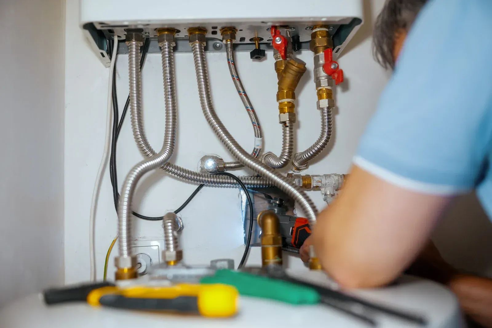 Person fixing a boiler with tools, metal pipes, and valves visible.