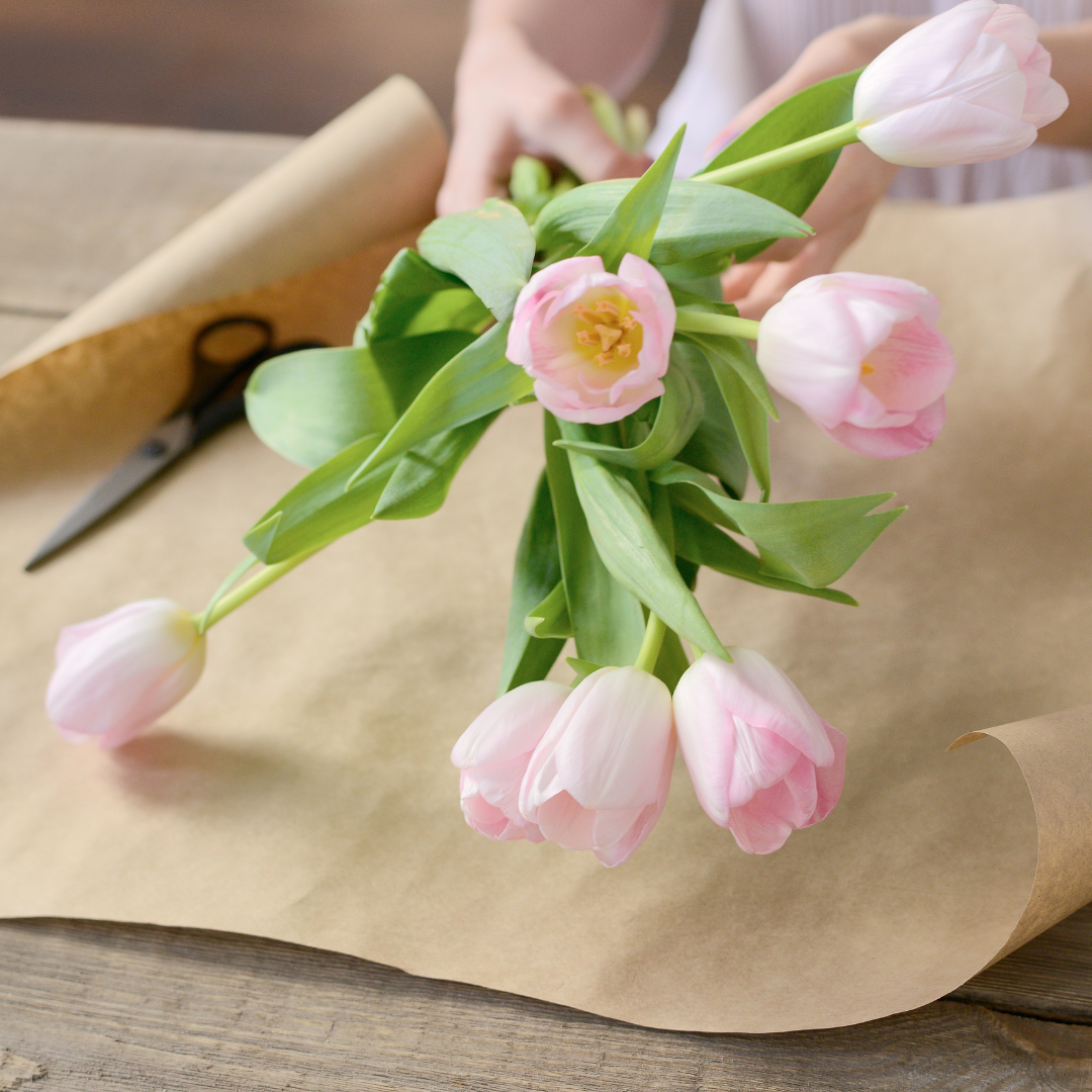 A person is wrapping a bouquet of pink flowers in brown paper