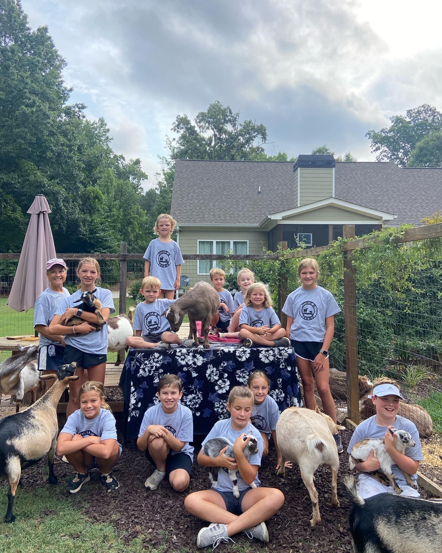 A group of children are posing for a picture with goats in front of a house.