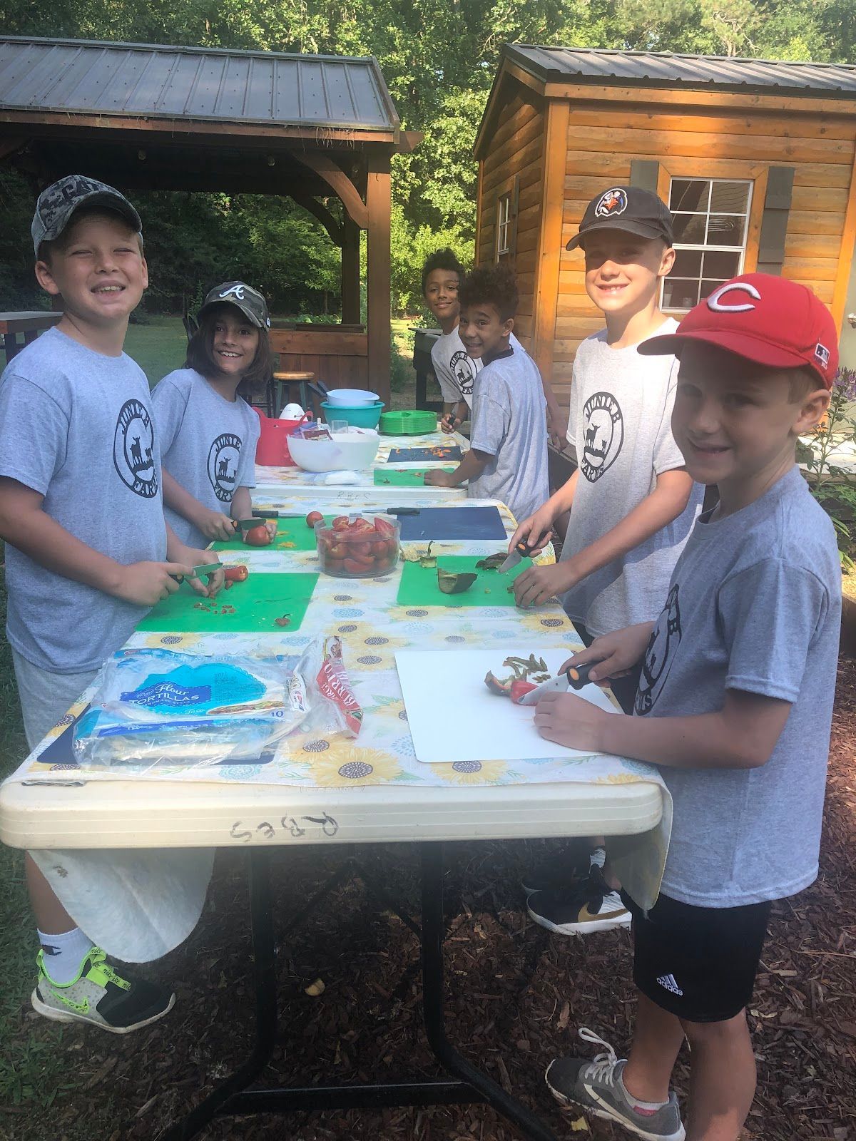 A group of children are standing around a table cutting vegetables.
