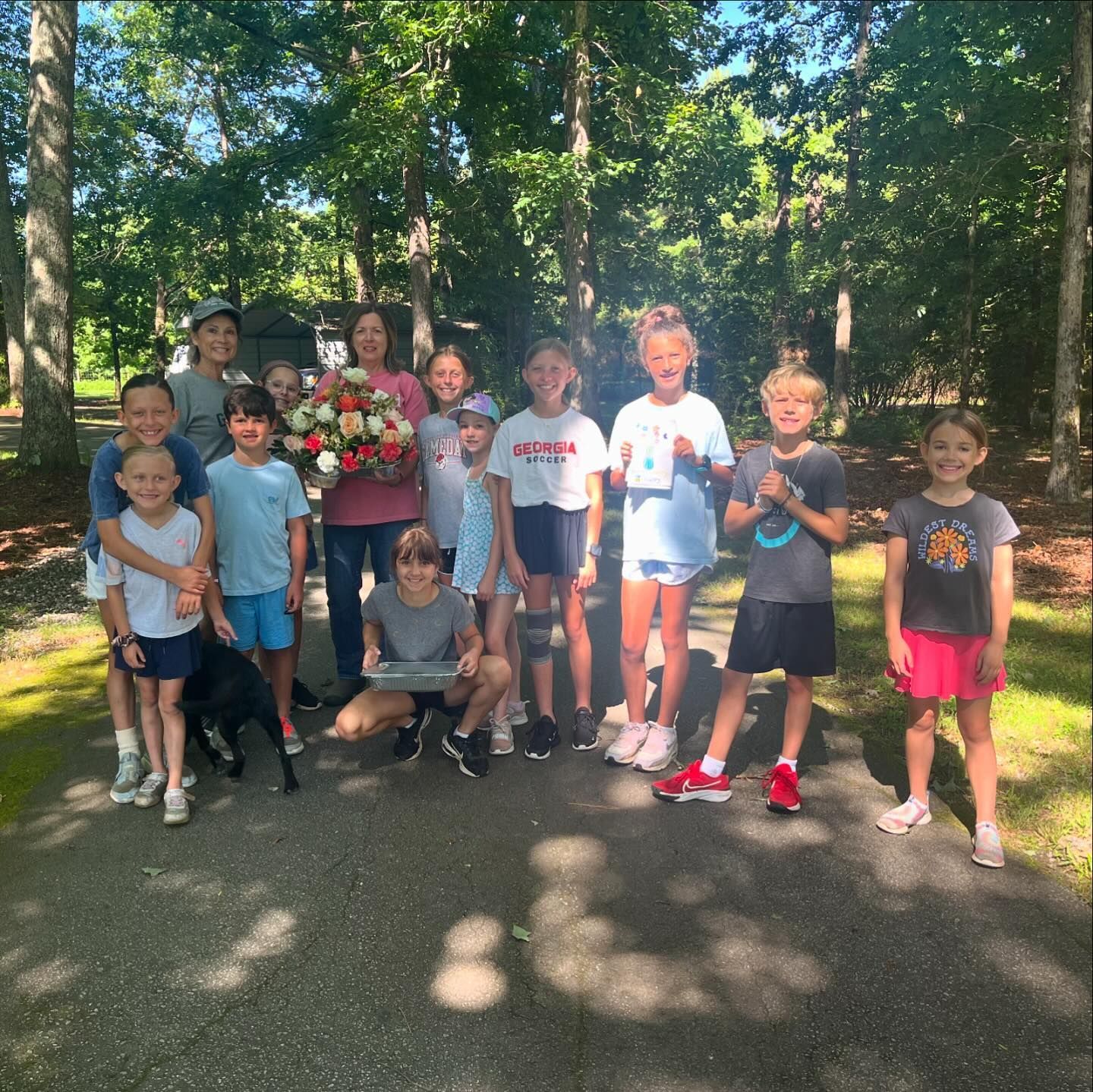 A group of children posing for a picture with a woman holding a bouquet of flowers