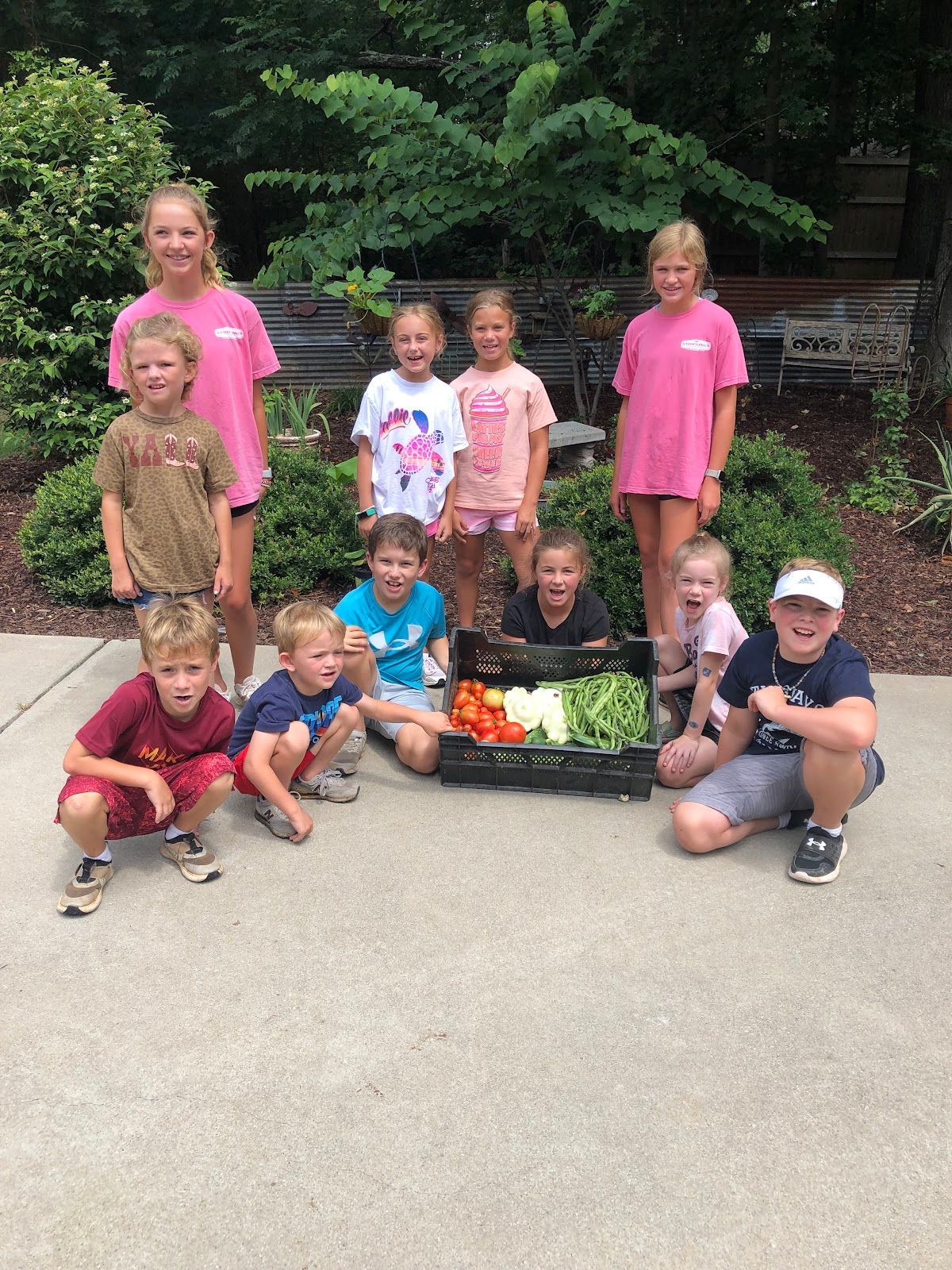 A group of children are posing for a picture with a crate of vegetables.
