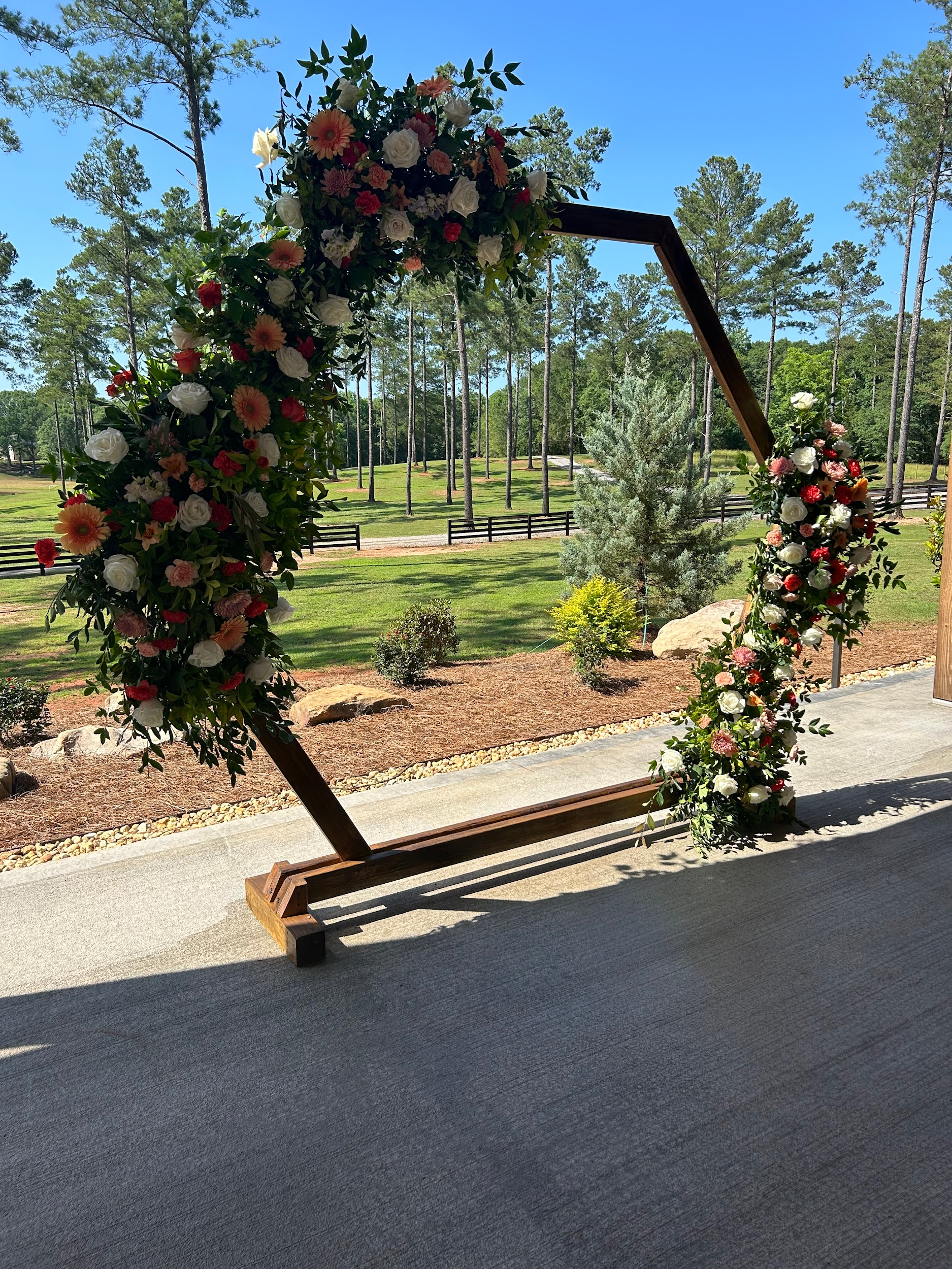 A wooden arch decorated with flowers is sitting on the side of a road.