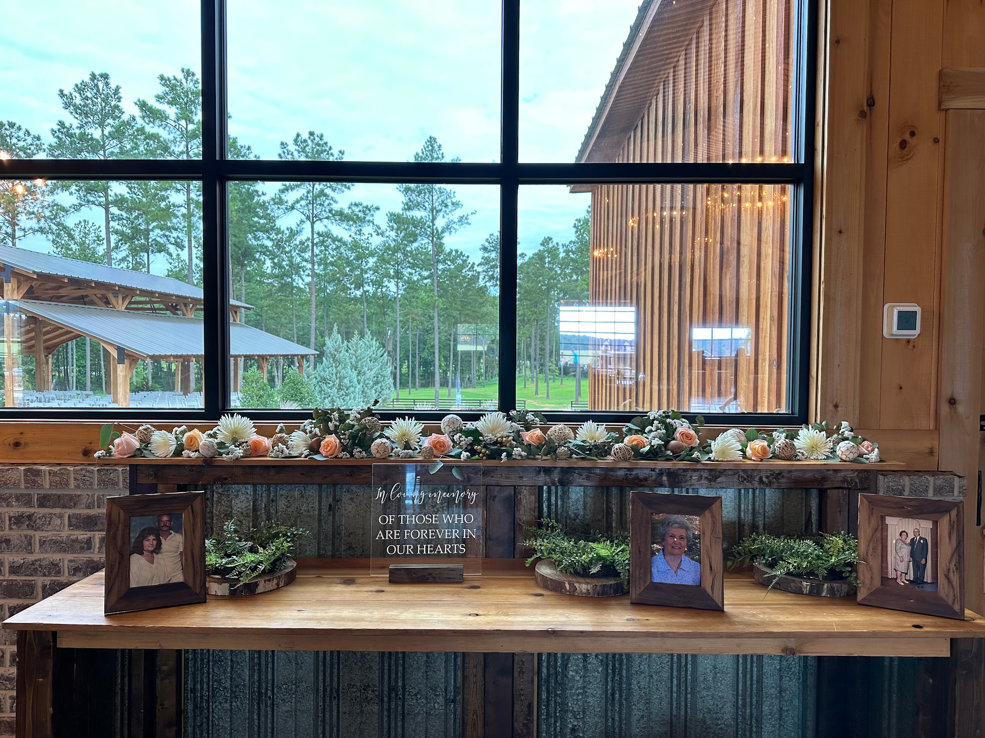 A wooden table with pictures and flowers on it in front of a large window.